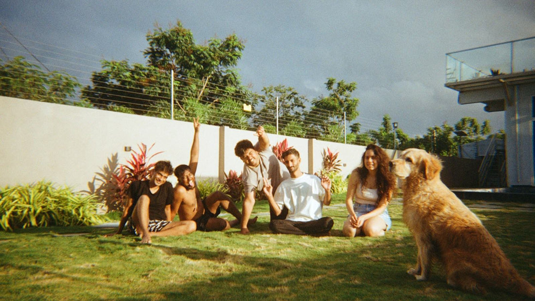 A group of friends sitting on the grass in a sunny backyard with their golden retriever beside them