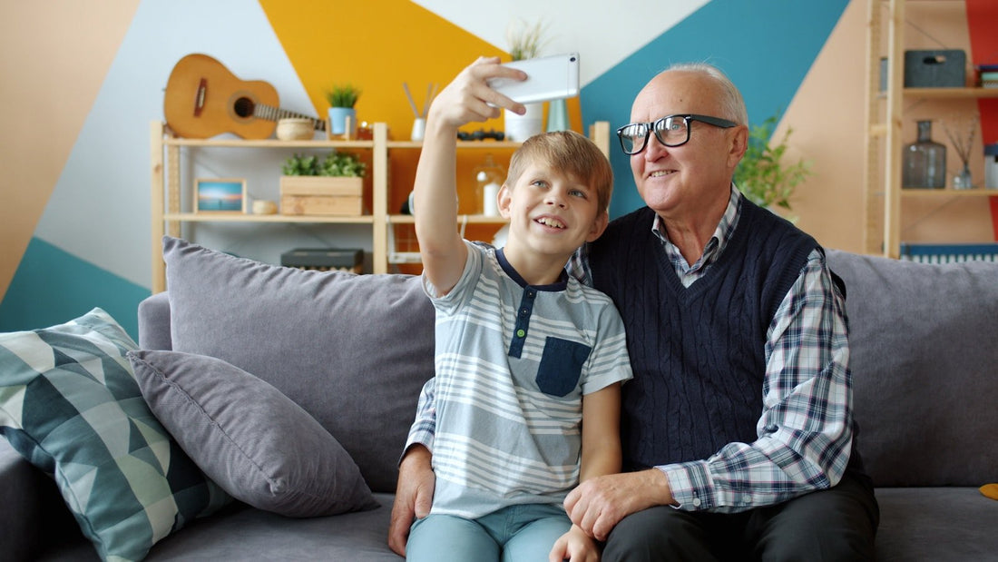 A grandfather and his grandson sitting on a couch at home, taking a selfie together