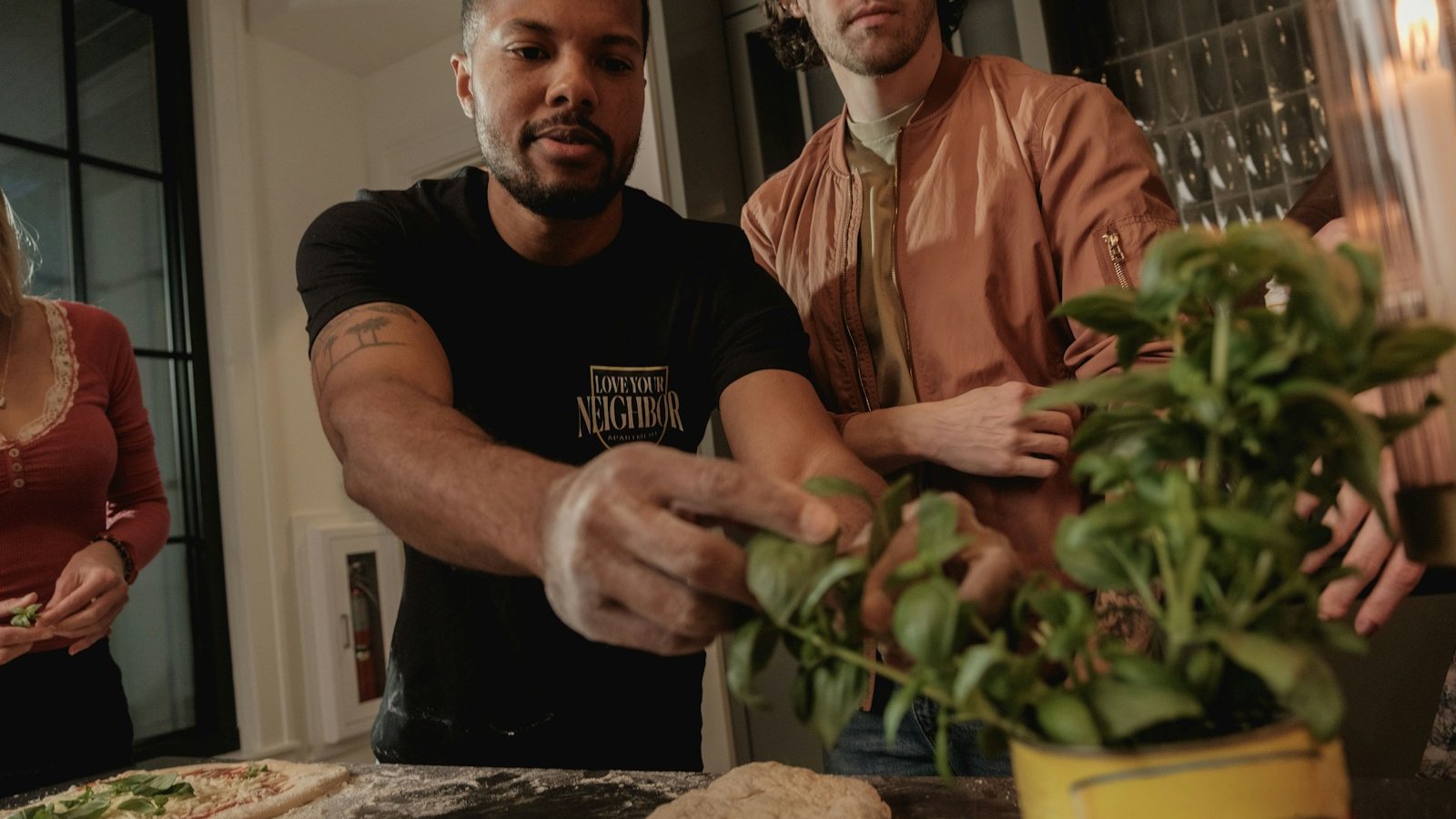 Two friends preparing homemade pizza with fresh basil at a kitchen counter