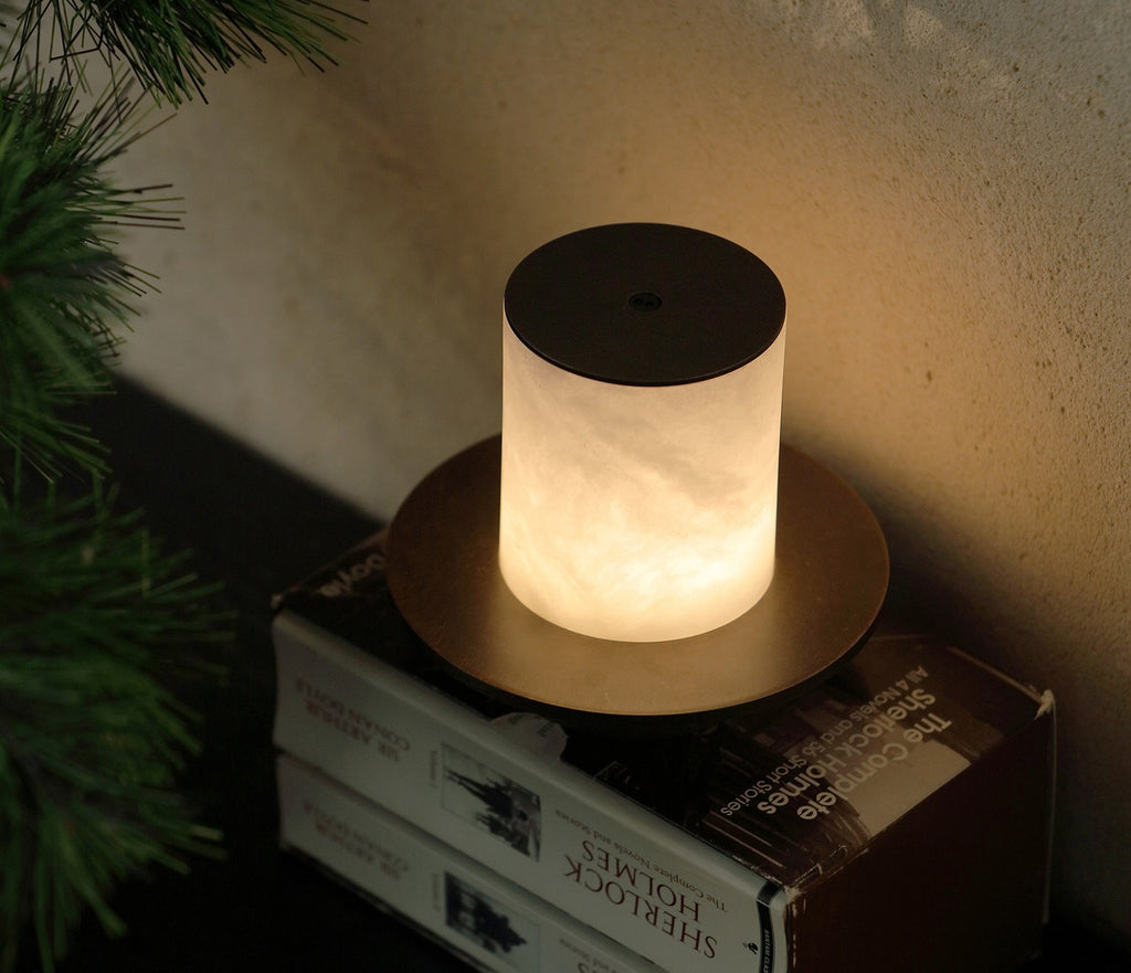 Warm alabaster lamp glowing beside books and pine in a cozy room