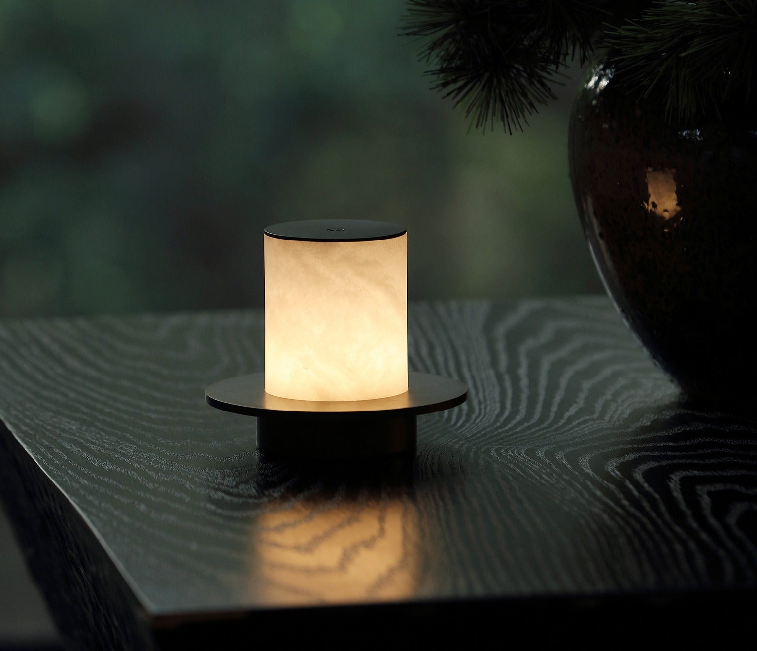 Cordless alabaster lamp lit on a dark wood table, natural stone veining
