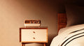 Retro walnut-grain Bluetooth speaker sitting on a wooden nightstand next to a bed in a warm bedroom