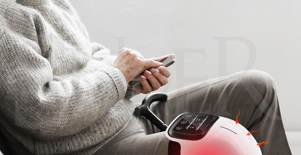 Older man in cream sweater scrolling his phone in an armchair while a Smart Knee Massager with red-light therapy warms his knee.
