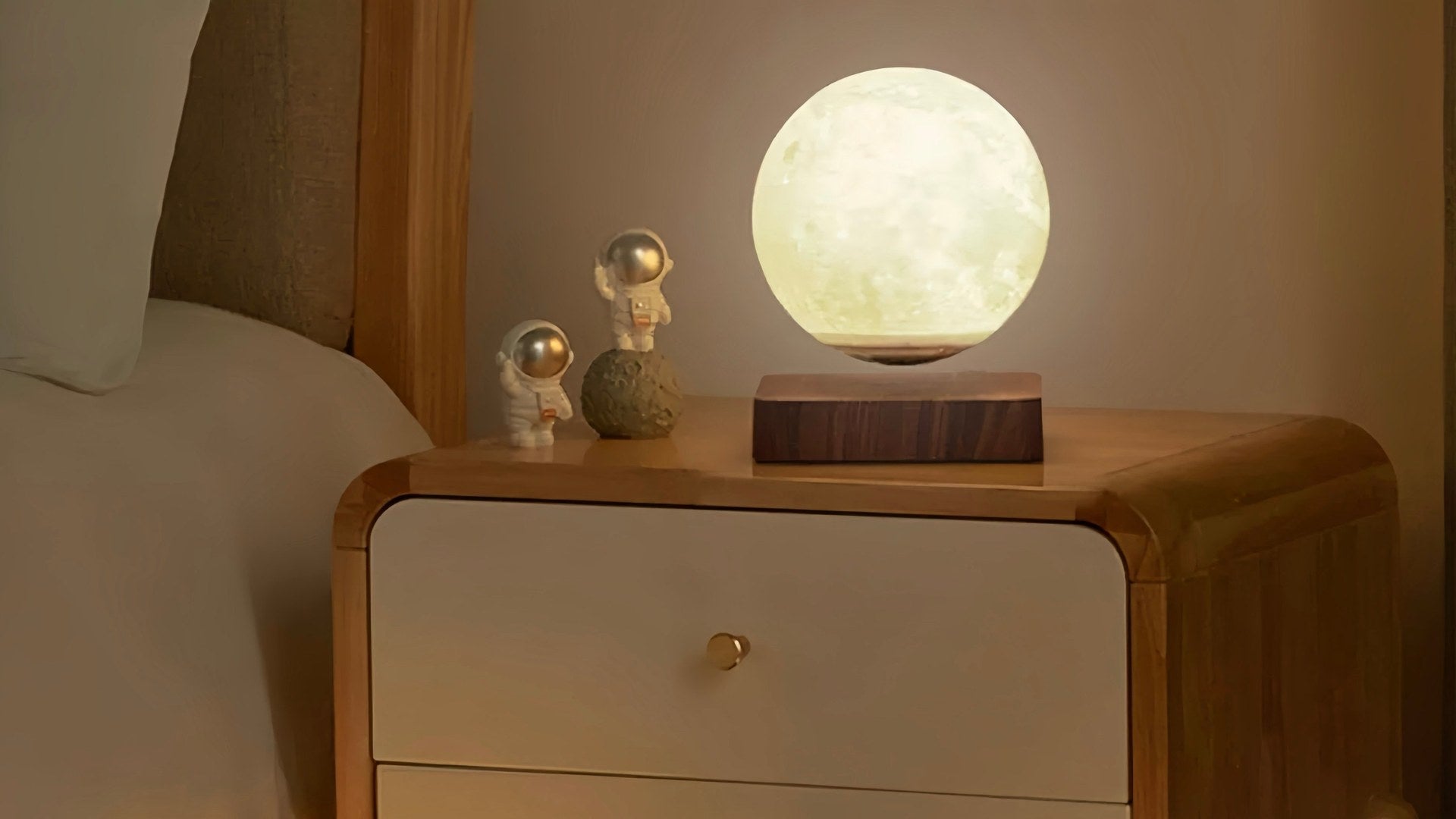 Levitating moon lamp magnetically floating above its walnut base on a bedside nightstand with astronaut figurines