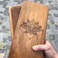 Handcrafted wooden Sadhu nail board with engraved lotus mandala held in a hand outdoors on a cobblestone street, with a second board behind it showing the metal nails on its acupressure surface